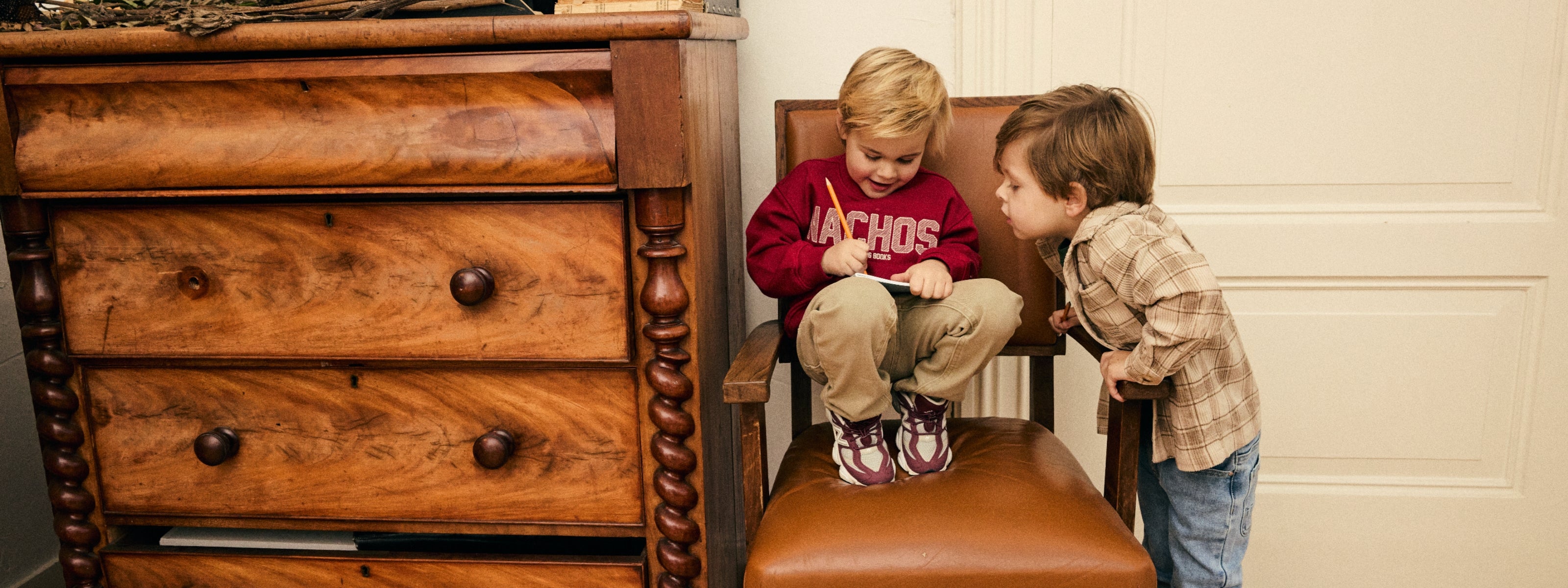 Twee jongens dragen een sweater en een geruit overshirt uit de Daily7 Kids collectie terwijl ze samen in een notitieboek kijken.