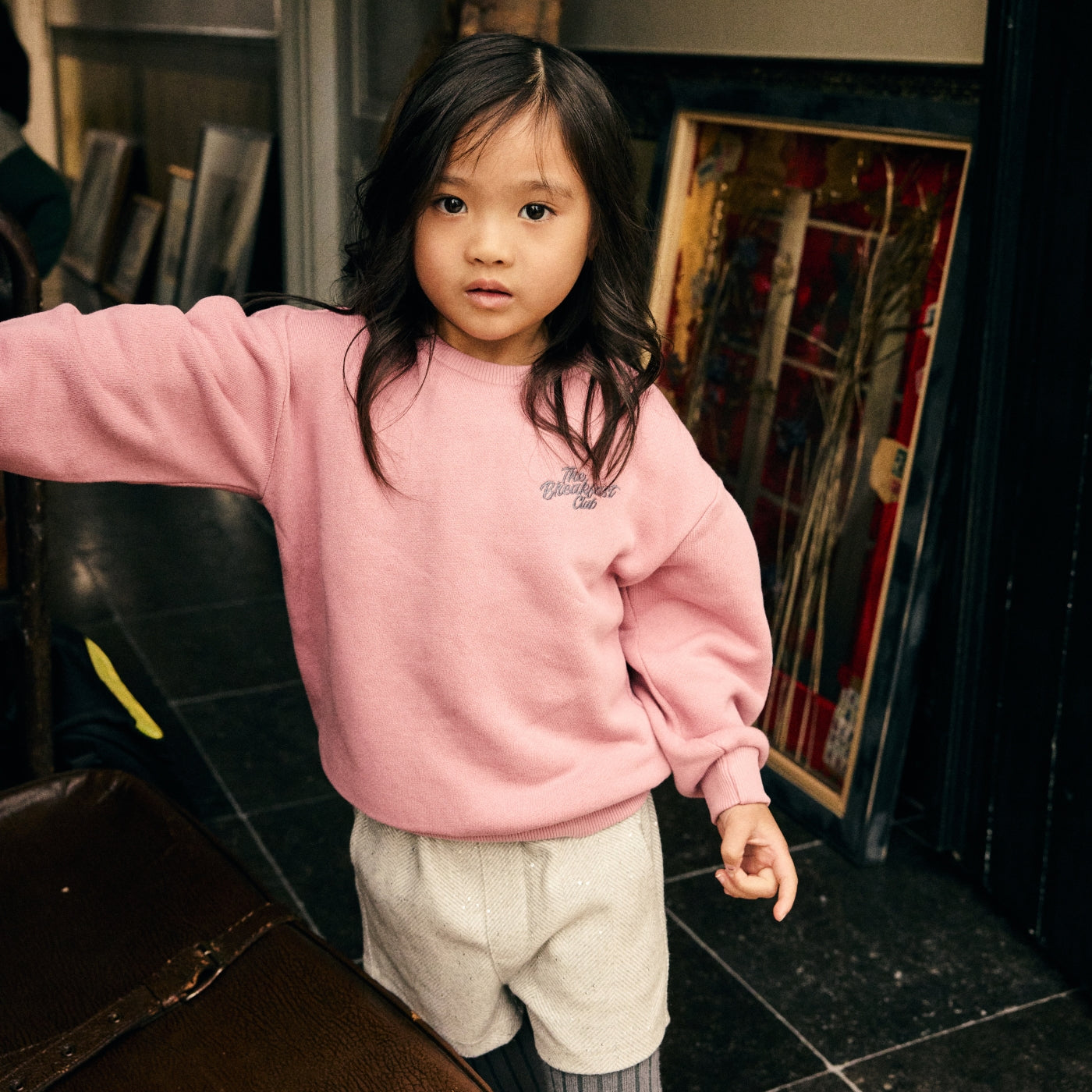 Meisje draagt een roze sweater en een lichte short uit de Daily7 Kids collectie in een warme, vintage geïnspireerde setting.