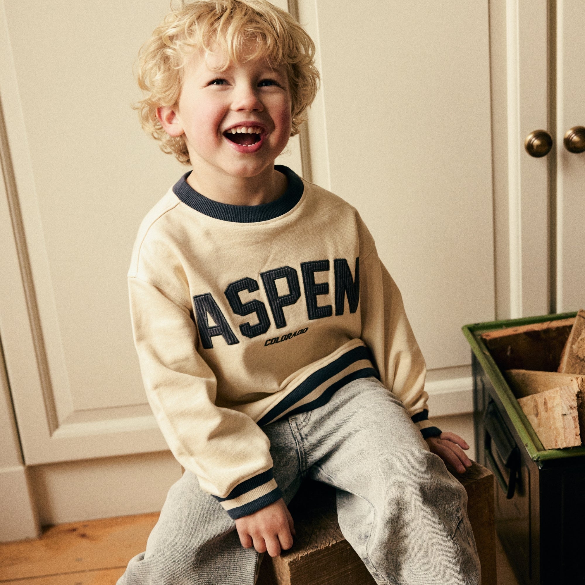 Jongen draagt een beige sweater met artwork en een lichtblauwe jeans uit de Daily7 Kids collectie.