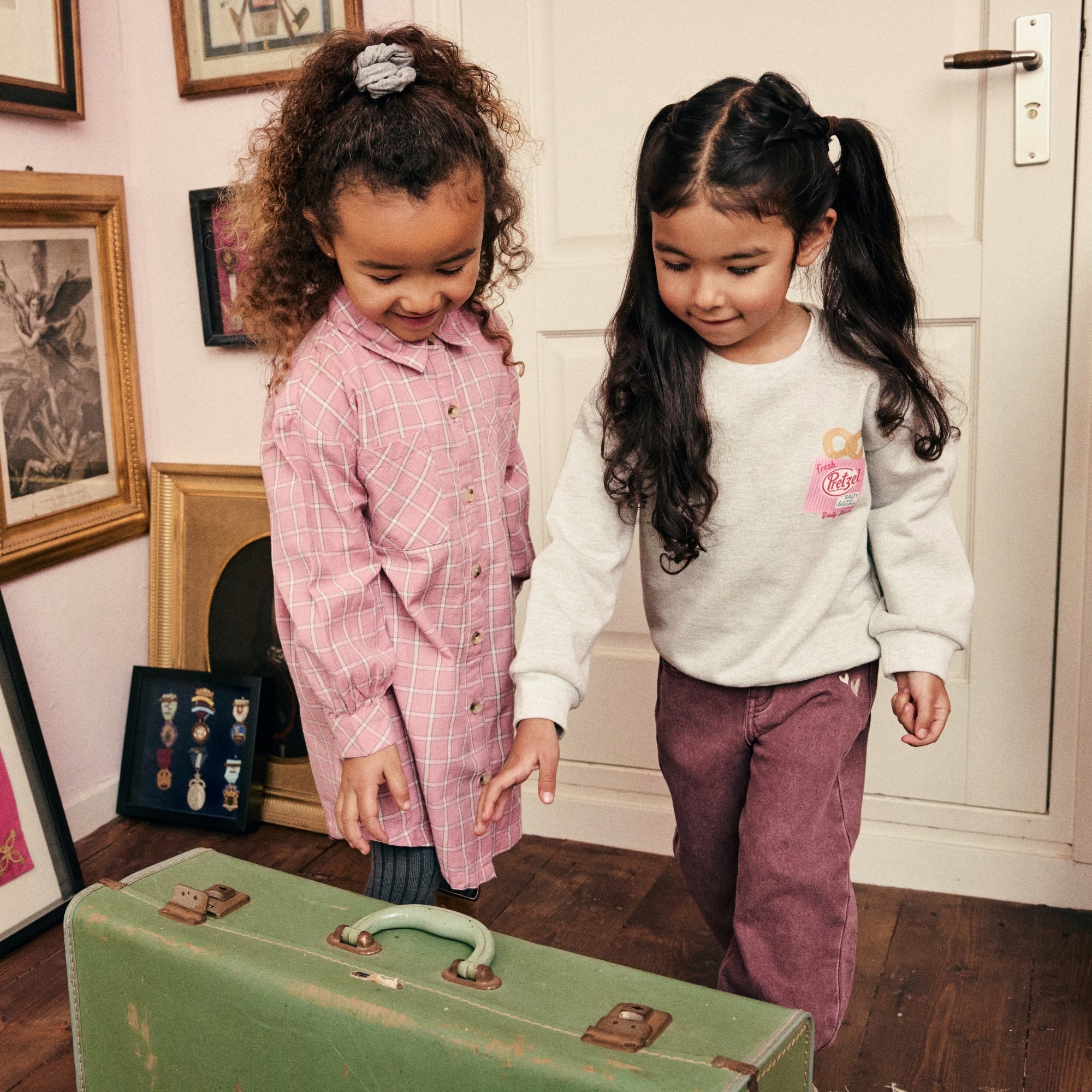 Twee meisjes dragen outfits uit de Daily7 Kids collectie en ontdekken een vintage koffer in een sfeervol interieur.