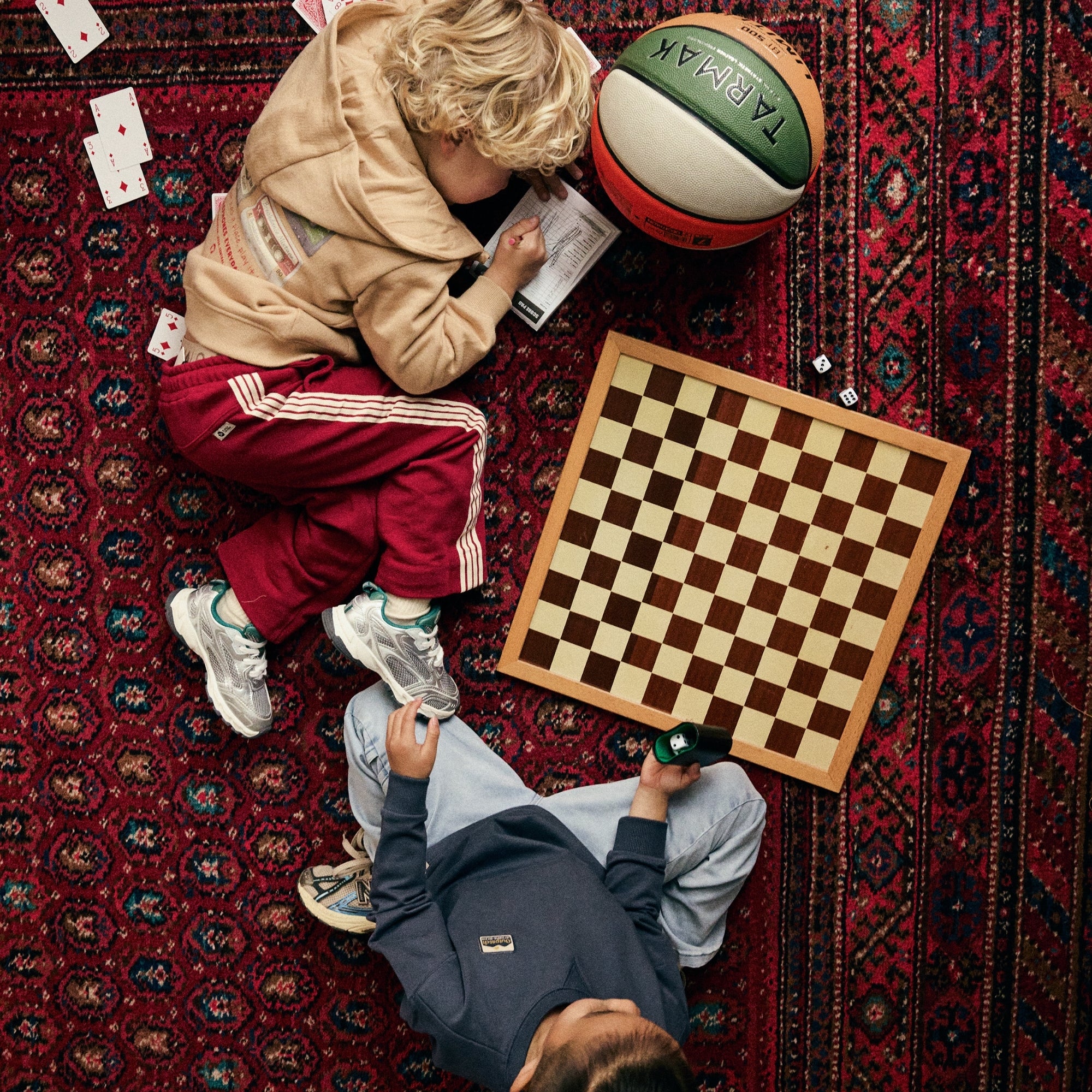 Twee jongens dragen outfits uit de Daily7 Kids collectie en spelen tussen een schaakbord, speelkaarten en een basketbal.